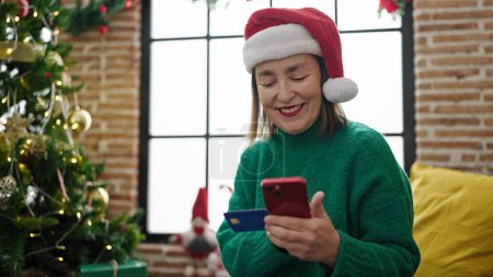 Téléchargez les photos : Femme hispanique mature aux cheveux gris faisant des achats en ligne de Noël avec smartphone à la maison - en image libre de droit