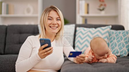 Téléchargez les photos : Achats mère et fille avec smartphone et carte de crédit assis ensemble à la maison - en image libre de droit