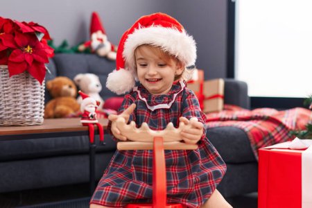 Photo for Adorable caucasian girl playing with reindeer rocking by christmas decoration at home - Royalty Free Image