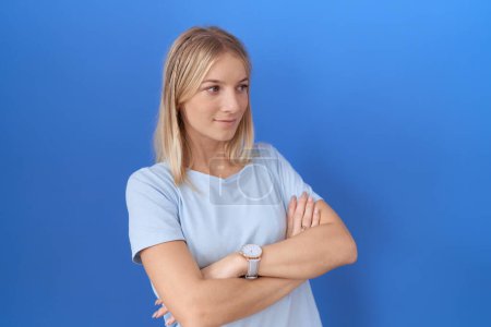 Foto de Joven mujer caucásica vistiendo casual camiseta azul mirando a un lado con los brazos cruzados convencida y confiada - Imagen libre de derechos