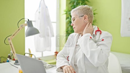 Foto de Médico mujer de pelo gris de mediana edad cansado estirando el cuello trabajando en la clínica - Imagen libre de derechos