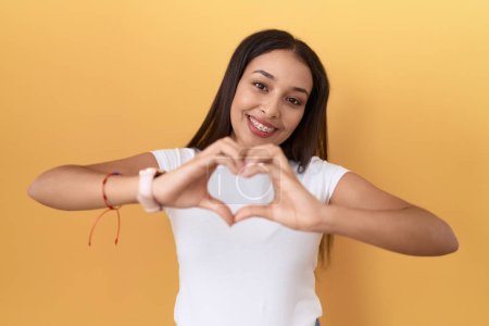 Photo for Young arab woman wearing casual white t shirt over yellow background smiling in love doing heart symbol shape with hands. romantic concept. - Royalty Free Image