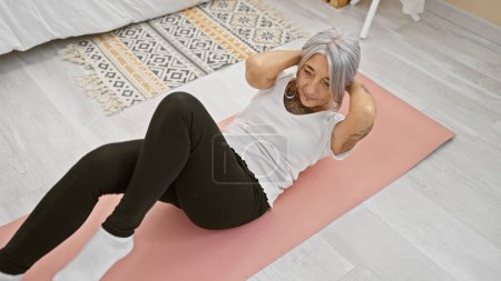 Photo for Middle age grey-haired woman training abs exercise at home - Royalty Free Image