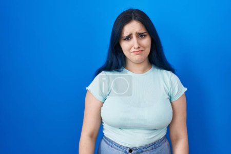 Photo for Young modern girl with blue hair standing over blue background depressed and worry for distress, crying angry and afraid. sad expression. - Royalty Free Image