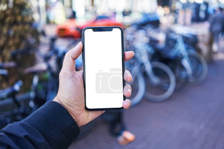 Téléchargez les photos : Homme tenant smartphone montrant écran blanc vierge au stationnement de vélo - en image libre de droit