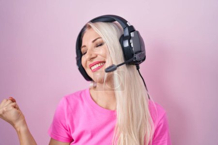 Téléchargez les photos : Femme caucasienne écoutant de la musique à l'aide d'écouteurs très heureux et excité de faire geste gagnant avec les bras levés, souriant et criant pour le succès. concept de célébration. - en image libre de droit