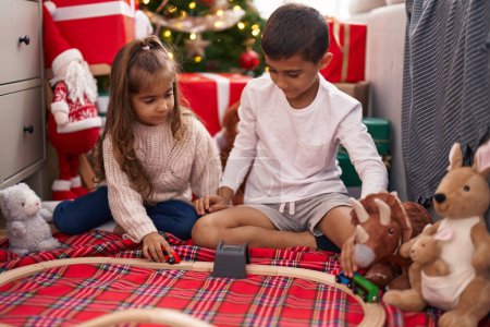 Photo for Brother and sister playing with cars sitting on floor by christmas gifts at home - Royalty Free Image