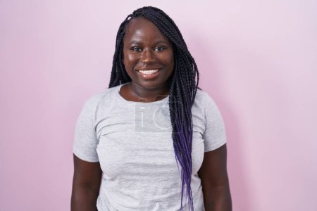 Foto de Mujer africana joven de pie sobre fondo rosa con una sonrisa feliz y fresca en la cara. persona afortunada. - Imagen libre de derechos