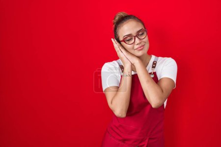 Photo for Young hispanic woman wearing waitress apron over red background sleeping tired dreaming and posing with hands together while smiling with closed eyes. - Royalty Free Image