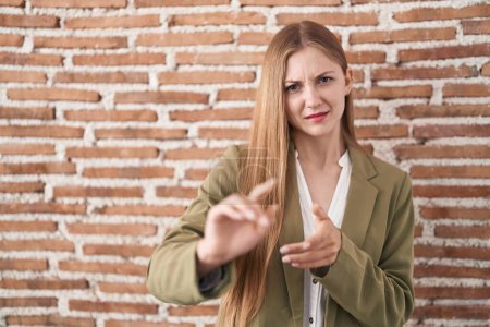 Téléchargez les photos : Young caucasian woman standing over bricks wall background disgusted expression, displeased and fearful doing disgust face because aversion reaction. with hands raised - en image libre de droit