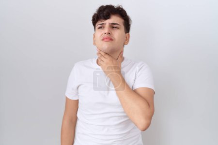 Foto de Hombre joven no binario con camiseta blanca casual tocando el cuello doloroso, dolor de garganta para la gripe, la clod y la infección - Imagen libre de derechos