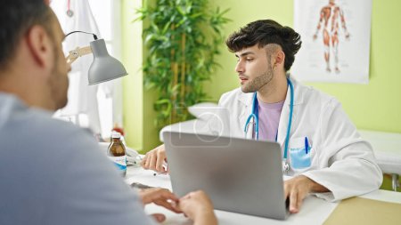 Téléchargez les photos : Deux hommes médecin et patient utilisant un ordinateur portable ayant une consultation à la clinique - en image libre de droit