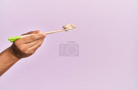 Téléchargez les photos : Main de l'homme tenant des pétoncles nigiri avec des baguettes sur fond rose isolé - en image libre de droit