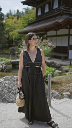 Photo for Cheerful young hispanic woman, effortlessly beautiful with glasses, confidently posing and joyfully smiling while exploring the serene surroundings of ginkaku-ji temple, kyoto, japan - Royalty Free Image