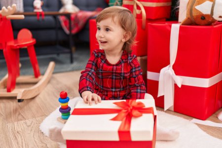 Foto de Adorable chica hispana desempacando regalo sentado en el suelo por árbol de Navidad en casa - Imagen libre de derechos