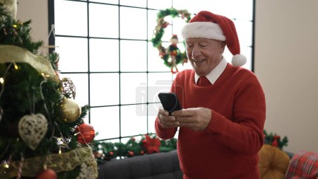 Photo for Senior using smartphone standing by christmas tree at home - Royalty Free Image