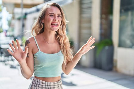 Téléchargez les photos : Jeune femme blonde souriante confiante parlant dans la rue - en image libre de droit