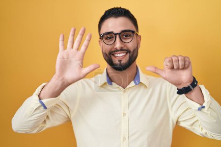 Foto de Joven hispano vistiendo ropa de negocios y gafas mostrando y señalando con los dedos número seis mientras sonríe confiado y feliz. - Imagen libre de derechos