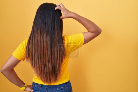 Téléchargez les photos : Jeune femme arabe debout sur fond jaune vers l'arrière pensant au doute avec la main sur la tête - en image libre de droit