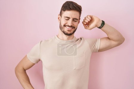Foto de Hombre hispano con barba de pie sobre fondo rosa que se extiende hacia atrás, cansado y relajado, soñoliento y bostezando por la mañana temprano - Imagen libre de derechos