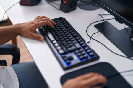 Téléchargez les photos : Jeune homme hispanique streamer jouer à un jeu vidéo en utilisant l'ordinateur à la salle de jeux - en image libre de droit