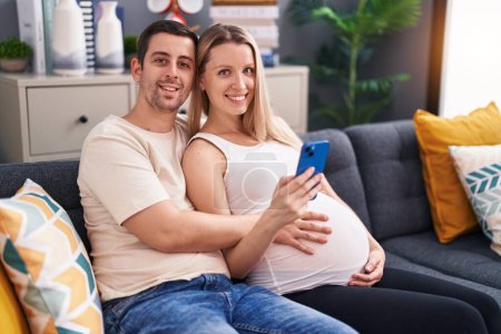 Téléchargez les photos : Homme et femme couple toucher le ventre en utilisant un smartphone à la maison - en image libre de droit