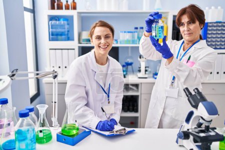 Photo for Two women scientists holding test tube writing on document at laboratory - Royalty Free Image