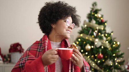 Photo for Young african american woman having breakfast standing by christmas tree at home - Royalty Free Image