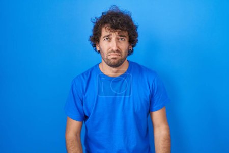 Photo for Hispanic young man standing over blue background depressed and worry for distress, crying angry and afraid. sad expression. - Royalty Free Image