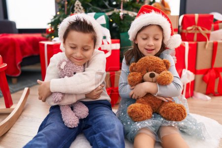 Téléchargez les photos : Adorable garçon et fille embrassant ours en peluche célébrant Noël à la maison - en image libre de droit