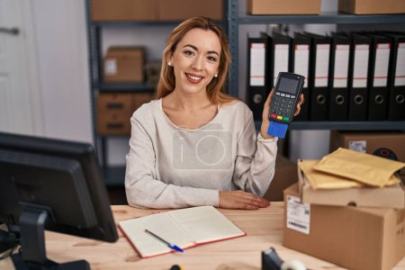 Téléchargez les photos : Femme hispanique travaillant dans une petite entreprise e-commerce tenant carte de crédit et dataphone regardant positif et heureux debout et souriant avec un sourire confiant montrant les dents - en image libre de droit