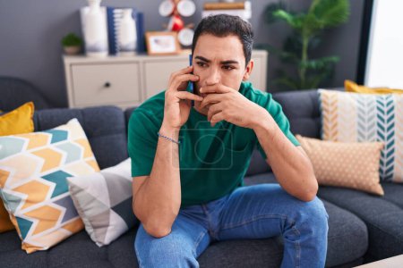 Photo for Young hispanic man talking on smartphone with worried expression at home - Royalty Free Image