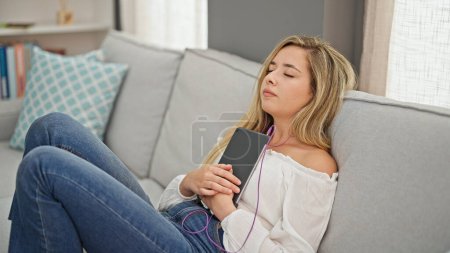 Téléchargez les photos : Jeune femme blonde écoutant de la musique dormir sur le canapé à la maison - en image libre de droit