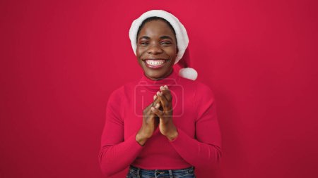 Téléchargez les photos : Femme afro-américaine portant chapeau de Noël applaudissements mains applaudissements sur fond rouge isolé - en image libre de droit