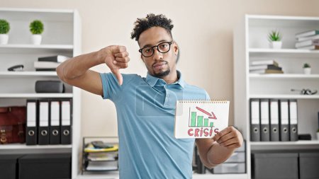 Foto de Trabajador de negocios afroamericano sosteniendo carta de crisis haciendo gesto de pulgar hacia abajo en la oficina - Imagen libre de derechos