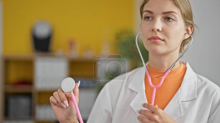 Téléchargez les photos : Jeune femme blonde médecin tenant stéthoscope examen à la clinique - en image libre de droit