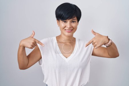 Foto de Joven mujer asiática con el pelo corto de pie sobre fondo aislado mirando confiado con sonrisa en la cara, señalándose con los dedos orgullosos y felices. - Imagen libre de derechos