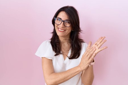 Téléchargez les photos : Femme hispanique du Moyen Âge portant T-shirt blanc décontracté et lunettes applaudissant et applaudissant heureux et joyeux, souriant mains fières ensemble - en image libre de droit