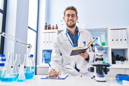 Photo for Young man scientist writing report reading book at laboratory - Royalty Free Image
