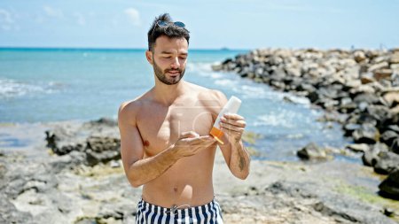 Foto de Joven turista hispano usando traje de baño aplicando protector solar en la playa - Imagen libre de derechos