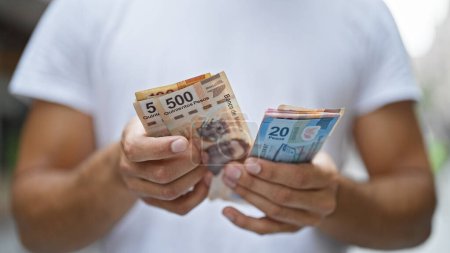 Téléchargez les photos : Jeune homme hispanique comptant les pesos mexicains dans la rue - en image libre de droit