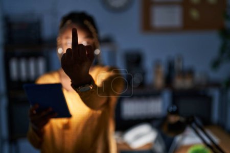 Photo for African american woman with braids working at the office at night with tablet showing middle finger, impolite and rude fuck off expression - Royalty Free Image