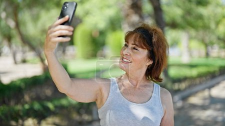 Téléchargez les photos : Femme d'âge moyen souriant confiant faire selfie par le smartphone au parc - en image libre de droit