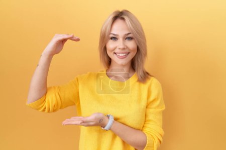 Photo for Young caucasian woman wearing yellow sweater gesturing with hands showing big and large size sign, measure symbol. smiling looking at the camera. measuring concept. - Royalty Free Image
