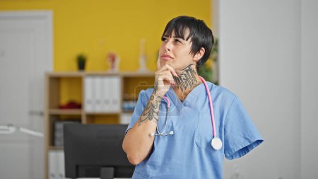Téléchargez les photos : Femme hispanique avec amputé bras médecin debout avec doute expression pensée à la clinique - en image libre de droit