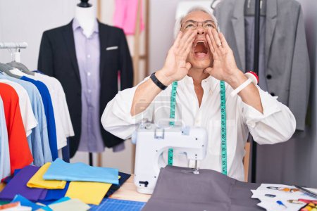 Photo for Middle age man with grey hair dressmaker using sewing machine shouting angry out loud with hands over mouth - Royalty Free Image