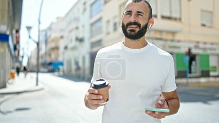 Téléchargez les photos : Jeune homme hispanique boire du café ayant les mains libres appel à la rue - en image libre de droit