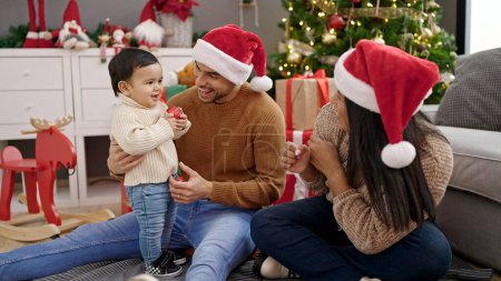 Téléchargez les photos : Couple et fils tenant boule de décoration assis sur le sol par arbre de Noël à la maison - en image libre de droit