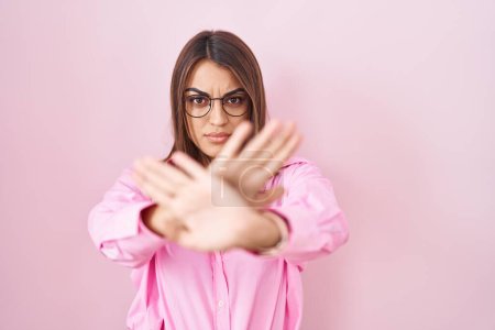 Téléchargez les photos : Jeune femme hispanique portant des lunettes debout sur fond rose expression de rejet croisement des bras et des paumes faisant signe négatif, visage en colère - en image libre de droit