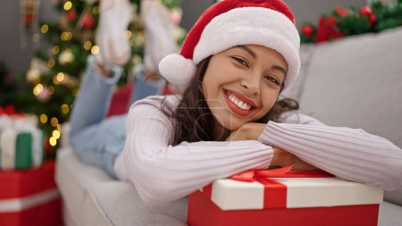 Téléchargez les photos : Jeune belle femme hispanique couchée sur le canapé avec cadeau de Noël à la maison - en image libre de droit